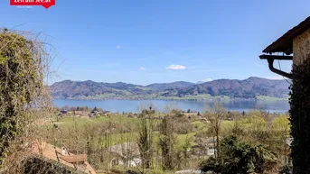 Panoramablick auf den See und die umliegende Berglandschaft unter blauem Himmel.