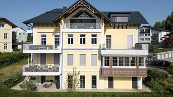 Elegantes Mehrfamilienhaus mit gelber Fassade, mehreren Balkonen und einer großzügigen Terrasse im Erdgeschoss.