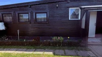 Dunkle Holzfassade eines Hauses mit kleinen Fenstern und einem gepflegten Vorgarten.