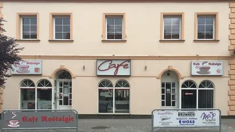 Fassade eines Cafés mit mehreren Fenstern und gewölbten Eingängen, beleuchteten Schildern und Straßensperren.