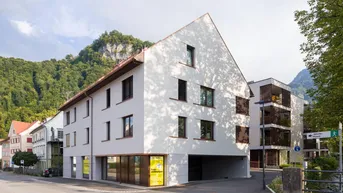 Mehrfamilienhaus mit moderner Architektur an einer Straße, umgeben von Bergen.