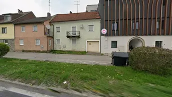 Ansicht der Gebäudefassade von der Straße aus mit angrenzendem modernen Bau und Balkon.