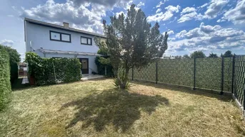 Gartenbereich hinter dem Haus mit Rasenfläche, einem Baum und einem Zaun unter blauem Himmel.