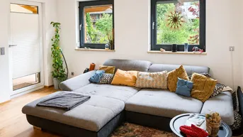 Gemütliches Wohnzimmer mit großem Ecksofa, Holzboden und Blick ins Grüne durch die Fenster.