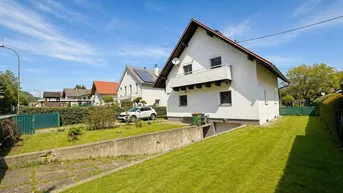 Einfamilienhaus mit Vorgarten, Auffahrt und Balkon unter blauem Himmel.