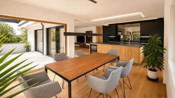 Moderner offener Wohn-Essbereich mit Holzboden, großer Küche und Zugang zu einer sonnigen Terrasse.