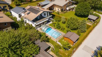Luftaufnahme eines Wohnhauses mit Garten, Pool und Photovoltaikanlage auf dem Dach.