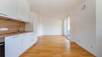 Heller offener Wohnbereich mit integrierter Küche, Holzboden und Zugang zu einem Balkon.
