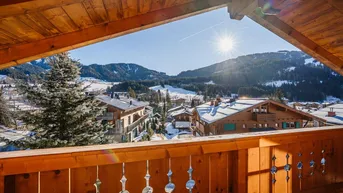 Sonniger Balkon mit weitem Blick über die verschneite Alpenlandschaft und die umliegenden Häuser.