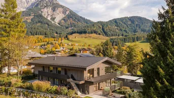 Modernes Holzchalet in alpiner Landschaft mit herbstlicher Vegetation und Bergblick.
