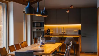 Moderne Küche mit dunklen Schränken, integrierten Geräten und Essbereich mit Holztisch.