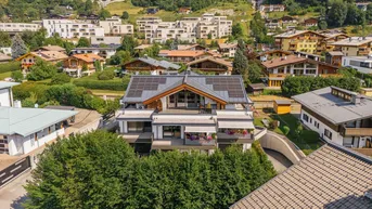 Moderne Wohnanlage mit Solarpaneelen auf dem Dach, eingebettet in eine grüne Hügellandschaft.