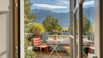 Gemütliche Terrasse mit Sitzgelegenheiten und atemberaubendem Bergblick unter blauem Himmel.