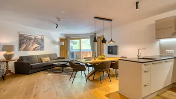 Geräumiger offener Wohn-Essbereich mit moderner Küche, Holzboden und Zugang zum Balkon mit Bergblick.