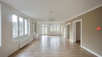 Geräumiges, helles Wohnzimmer mit Parkettboden, großen Fenstern und einem eleganten Kronleuchter.