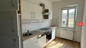 Helle Einbauküche mit weißen Schränken, Holzoptik-Arbeitsplatte und Fenster mit Blick ins Grüne.