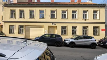 Gelbes Gebäude mit mehreren Fenstern und einer Garageneinfahrt an einer städtischen Straße.