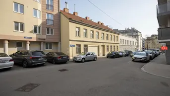 Ansicht der Gebäudefassade von der Straße aus mit parkenden Autos und umliegenden Gebäuden.