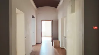 Heller Flur mit Holzboden, hohen Decken und Durchgang zu weiteren Räumen.