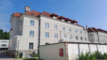 Ansicht eines gepflegten Mehrfamilienhauses mit rotem Ziegeldach und Gaubenfenstern unter blauem Himmel.