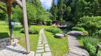 Weitläufiger Gartenbereich mit Steinpfad, Rasenflächen, Teich und umgebender Natur.