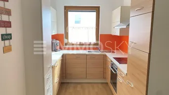 Funktionale Küche mit hellen Holzfronten, orangefarbenem Fliesenspiegel und Fenster über der Spüle.