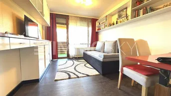 Gemütliches Wohnzimmer mit dunklem Laminatboden, hellen Möbeln und Zugang zum Balkon.
