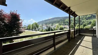 Geräumiger Balkon mit Holzboden und schöner Aussicht auf die umliegende Berglandschaft und das Dorf.