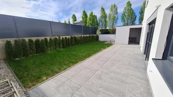 Gepflasterte Terrasse mit Rasenfläche und Hecke im Gartenbereich eines modernen Hauses.