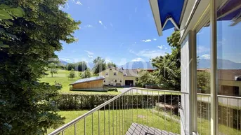 Blick vom Balkon mit Holzboden und Metallgeländer auf grüne Landschaft und Berge.