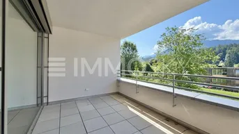 Heller Balkon mit Fliesenboden und weitem Blick auf die umliegende grüne Landschaft und Berge.