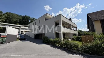 Moderne Wohnanlage mit mehreren Etagen, Balkonen und Zufahrt zur Tiefgarage, umgeben von viel Grün.