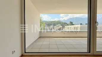 Heller Innenraum mit Holzboden und großem Fenster, das auf eine Terrasse mit Bergblick führt.