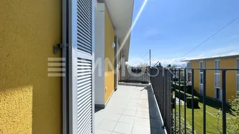 Heller Balkon mit Fliesenboden, gelber Fassade und Blick ins Grüne an einem sonnigen Tag.