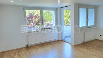 Helles, unmöbliertes Wohnzimmer mit Parkettboden, großen Fenstern und Zugang zum Balkon.