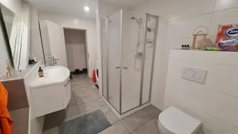 Modernes Badezimmer mit Duschkabine, Waschbecken und Toilette, hell gefliest.