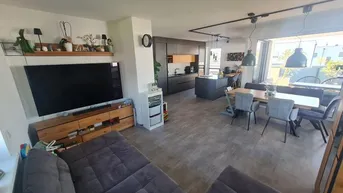 Heller, offener Wohn-Essbereich mit integrierter Küche, modernem Sofa und großem Esstisch.