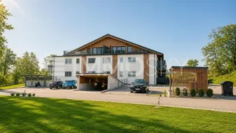 Modernes Mehrfamilienhaus mit Tiefgaragenzufahrt, Außenparkplätzen und gepflegter Grünfläche.