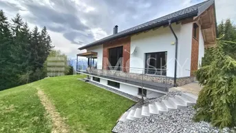 Modernes Haus in Hanglage mit großem Garten, Balkon und Bergblick unter bewölktem Himmel.