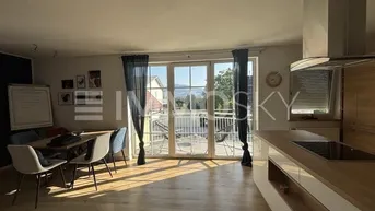 Heller offener Wohn- und Essbereich mit Holzboden, moderner Küche und Zugang zum Balkon mit Weitblick.