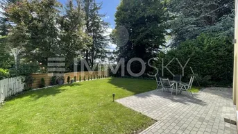 Gepflegter Gartenbereich mit großer gepflasterter Terrasse und Sitzgelegenheiten im Freien, umgeben von Bäumen.