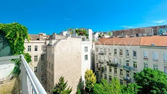 Blick von einem Balkon auf umliegende Gebäude und grüne Bäume unter blauem Himmel.