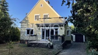 Freistehendes Haus mit gelber Fassade, Balkon, Garten und gepflasterter Einfahrt.