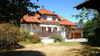 Einfamilienhaus mit rotem Ziegeldach, Balkon und Photovoltaikanlage auf dem Nebengebäude.