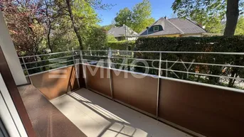 Heller Balkon mit Metallgeländer und Blick ins Grüne sowie auf umliegende Häuser.