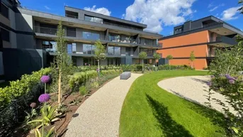 Gepflegte Gartenanlage mit Kieswegen, Rasenflächen und modernen Wohngebäuden im Hintergrund.