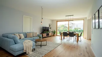 Heller offener Wohn- und Essbereich mit modernem Sofa, Holzboden und direktem Zugang zum Garten.