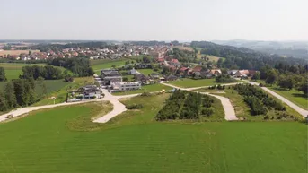 Luftaufnahme einer ländlichen Gegend mit einem Dorf im Hintergrund und grünen Feldern.