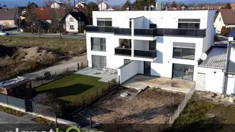 Luftaufnahme einer modernen Wohnanlage mit weißer Fassade, Balkonen und einem Gartenbereich.