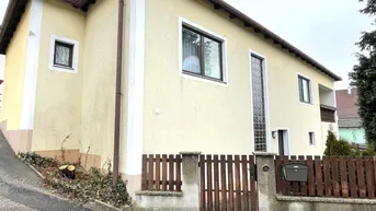 Gelbe Fassade eines Einfamilienhauses mit braunem Holzzaun und gepflegtem Vorgarten.